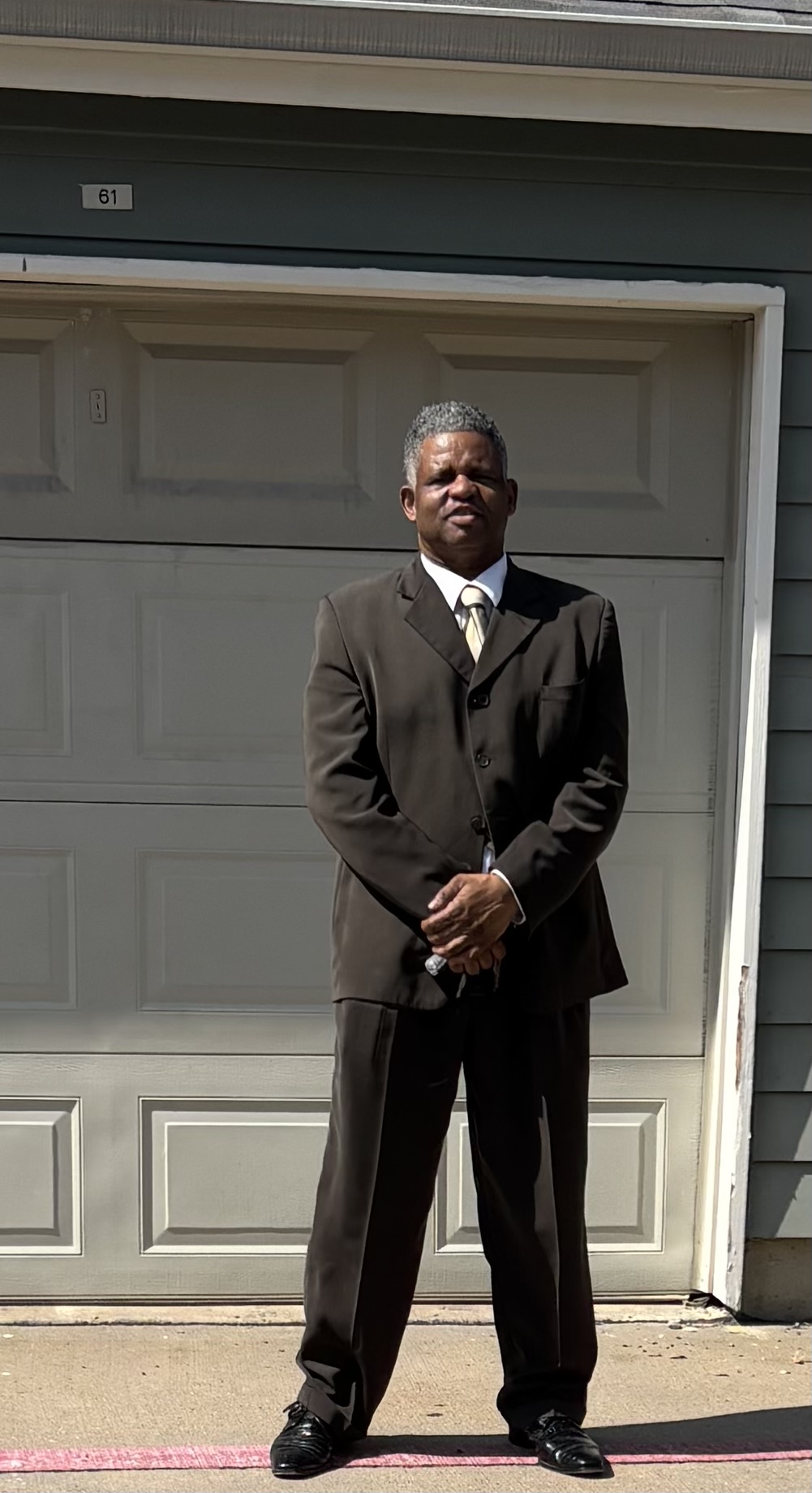 Professional man in dark suit and tie standing in front of garage door number 61