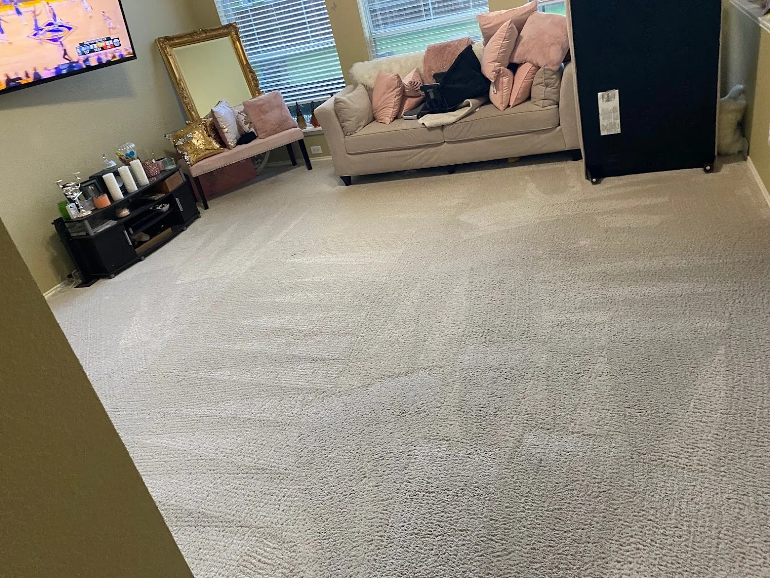 Modern living room with beige carpet, tan sofa with pink pillows, black media console, and windows with blinds