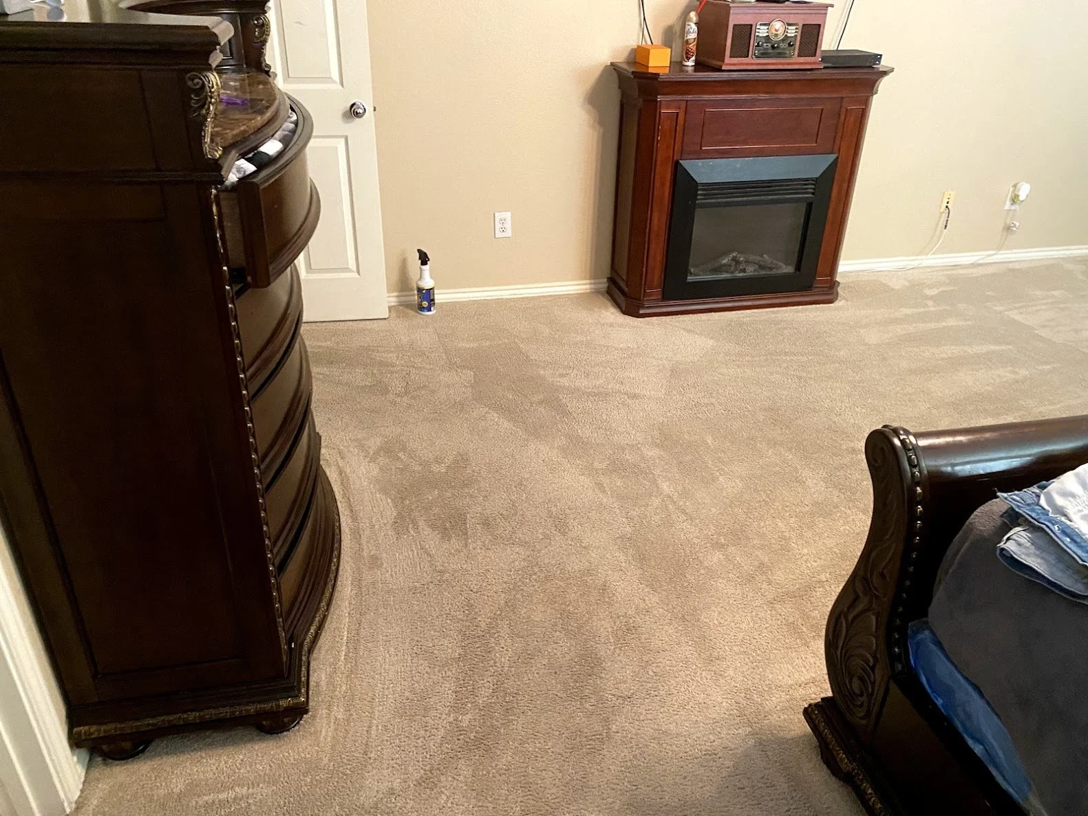 Spacious bedroom with beige carpet, dark wood furniture including dresser and fireplace mantel, cream walls