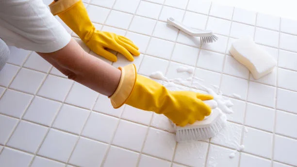Person in yellow gloves scrubbing white tile floor with brush