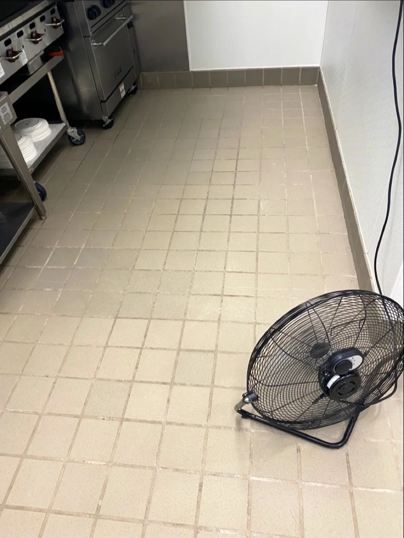 Commercial kitchen with tile floor, industrial equipment, and black floor fan